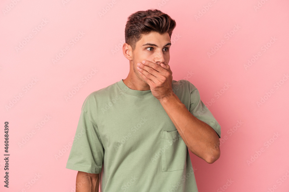 Young caucasian man isolated on pink background thoughtful looking to a copy space covering mouth with hand. Young caucasian man isolated on pink background thoughtful looking to a copy space covering mouth with hand.