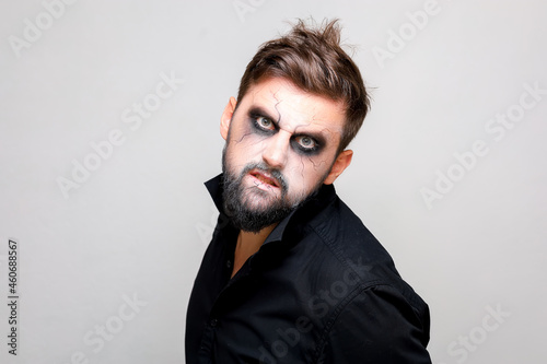 a bearded man with undead-style makeup on Halloween looks with big eyes at the camera © Roman