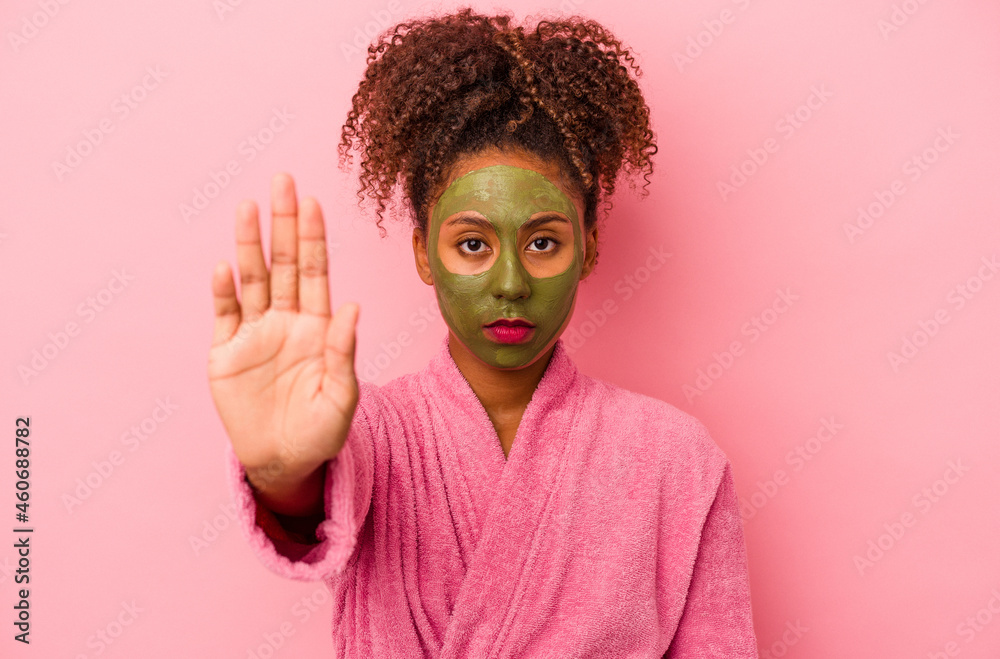 Young african american woman wearing a bathrobe and facial mask isolated on pink background standing with outstretched hand showing stop sign, preventing you. Young african american woman wearing a bathrobe and facial mask isolated on pink background standing with outstretched hand showing stop sign, preventing you.