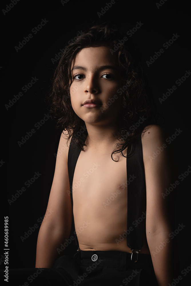 Hermoso niño sin camisa viendo a cámara en estudio con fondo negro Hermoso niño sin camisa viendo a cámara en estudio con fondo negro
