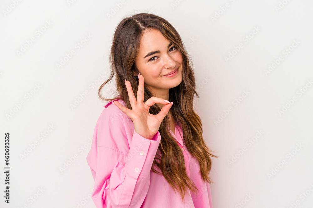 Young caucasian woman isolated on white background winks an eye and holds an okay gesture with hand.