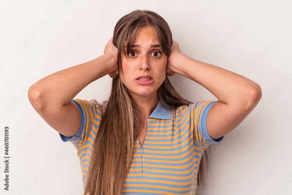 Young caucasian woman isolated on white background covering ears with hands trying not to hear too loud sound.