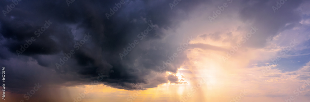 Dramatic sky panorama with bright sun shining through the dark rainy clouds.