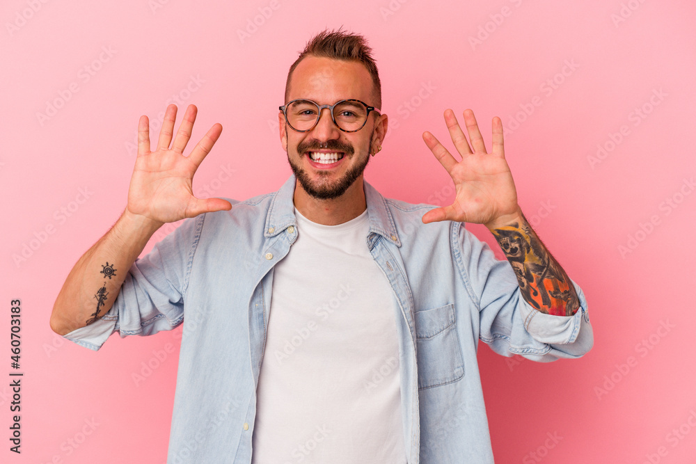 Young caucasian man with tattoos isolated on pink background showing number ten with hands. Young caucasian man with tattoos isolated on pink background showing number ten with hands.