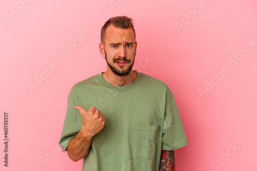 Young caucasian man with tattoos isolated on pink background shocked pointing with index fingers to a copy space.