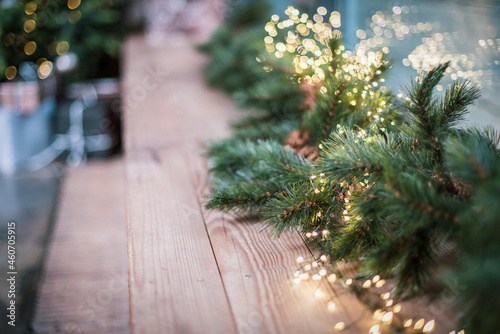 Spruce branches with a glowing Christmas garland decorate the windowsill. Christmas tree and gifts on the background.