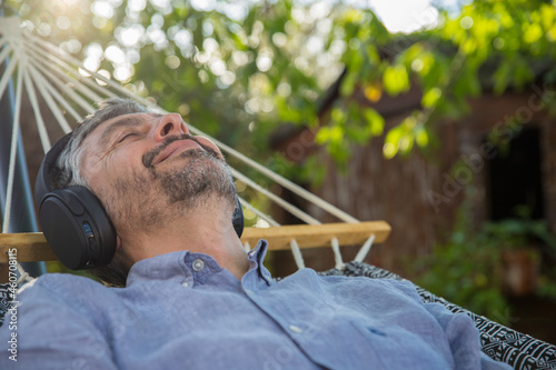 Homme d'âge mur 50 ans se repose dans son hamac en écoutant de la musique avec un casque à l'ombre d'un arbre. Il profite de la vie