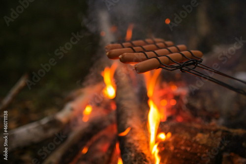 Sausages are fried on a grill by the fire.