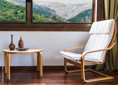 Rocking chair and small table next to a window with a mountain view