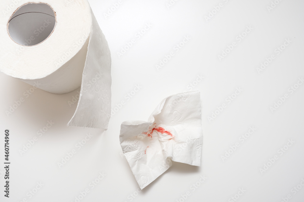Used sheet of bloody toilet paper and a roll on white background