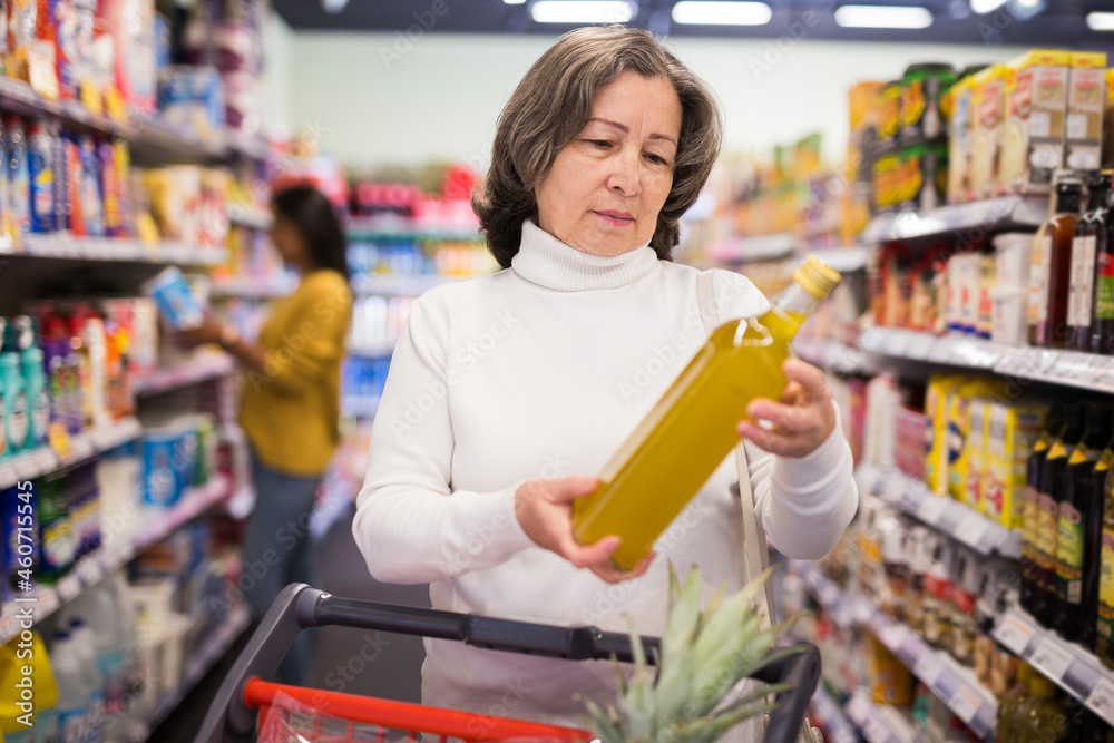 Elderly shopper chooses olive oil at grocery supermarket