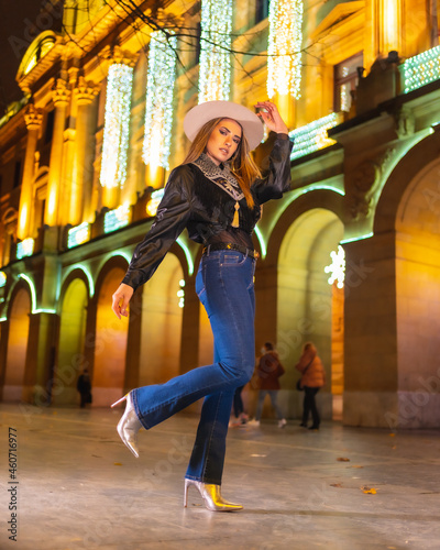 Winter lifestyle, Caucasian blonde girl wearing jeans and black jacket in the city illuminated for christmas at night, vertical photo © unai