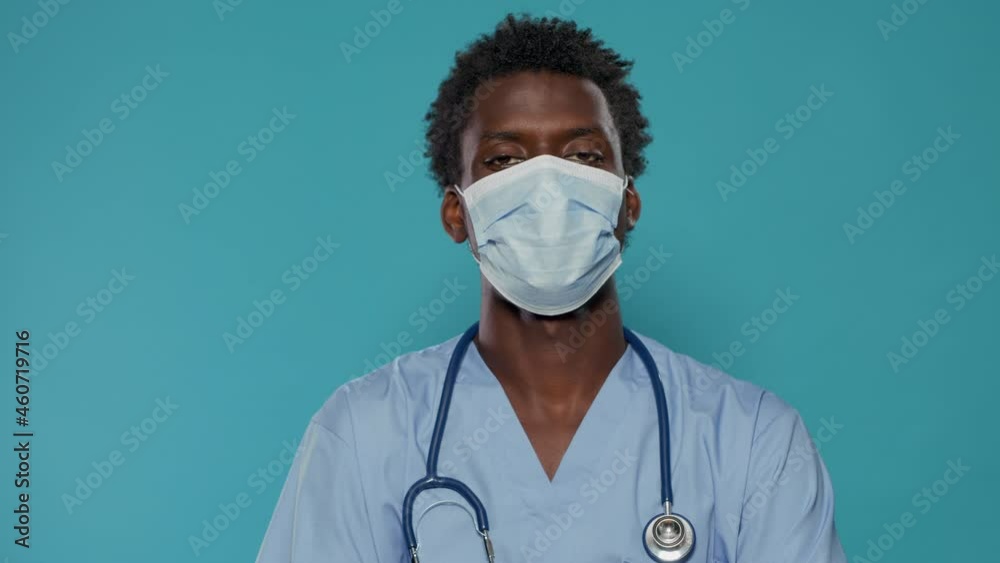 Close up of medical assistant with face mask looking at camera in studio. Portrait of man working as nurse, wearing blue uniform and stethoscope while having protection against covid 19 Close up of medical assistant with face mask looking at camera in studio. Portrait of man working as nurse, wearing blue uniform and stethoscope while having protection against covid 19