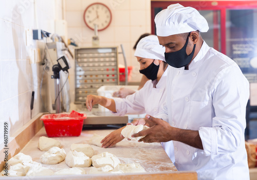 Professional hispanic baker standing at work table, kneading and forming dough for baking bread