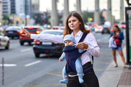 Mother with baby in sling is stopping taxi near traffic.