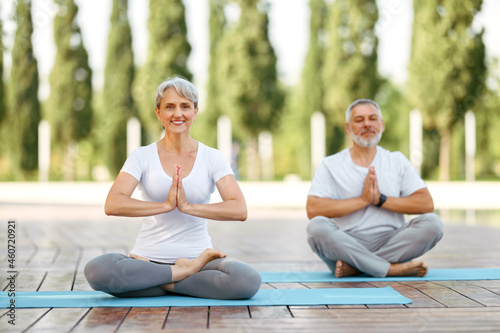 Happy senior husband and wife meditating in lotus position during yoga outdoors