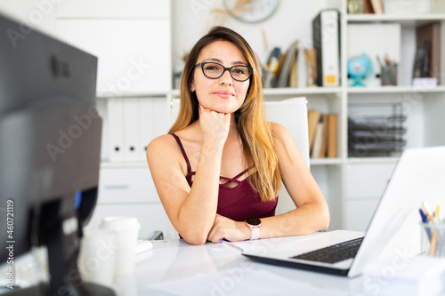 Young colombian woman in glasses working with laptop at the office table