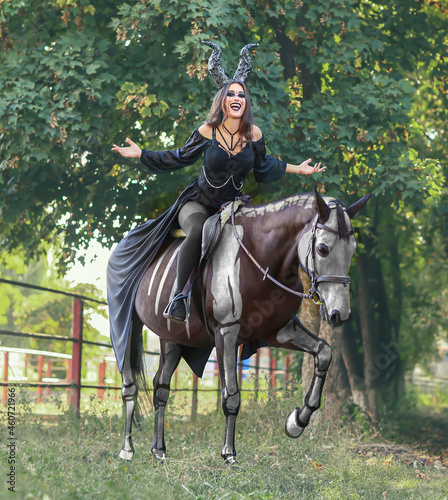 Beautiful woman dressed for Halloween with horse painted as skeleton outdoors