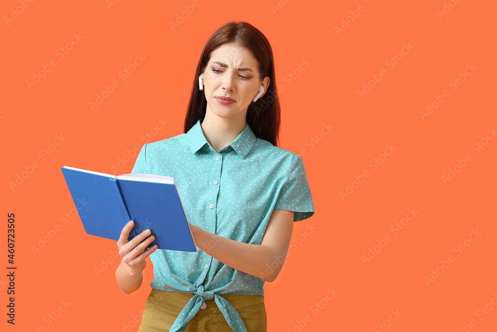 Displeased young woman with earphones and book on color background