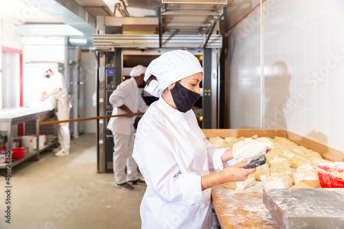 Bakery worker cuts raw dough with a knife