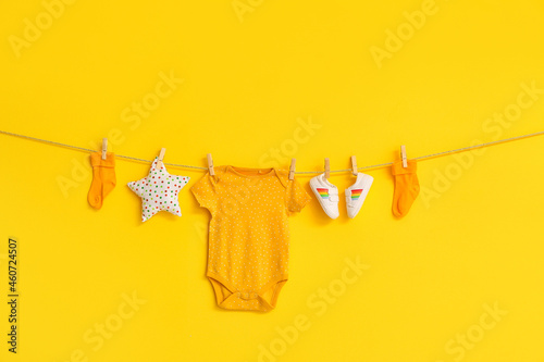 Stylish baby clothes, shoes and toy hanging on rope against color background photo