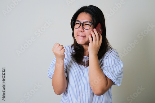 Adult Asian woman showing angry face expression while answering a phone call photo