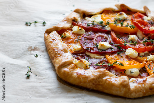 A multi colored heirloom tomato galette with thyme and feta cheese on parchment paper