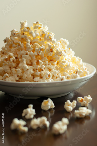 Overflowing white bowl of buttery popcorn on a dark table against a light beige wall