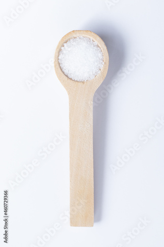A single wooden measuring spoon of kosher salt isolated on a plain white background with a light shadow. 