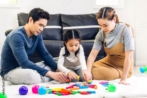 Portrait of enjoy happy love asian family father and mother with little asian girl smiling play with toy build wooden block board game in moments good time at home