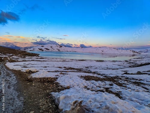 Ice lake in snow covered ground with small stones placed on the ground with orange clouds in blue sky and hills covered with snow