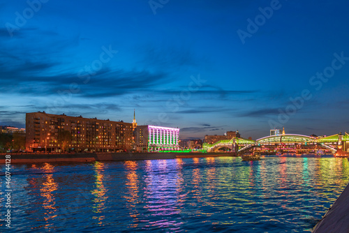 View of the colorful Bogdan Khmelnitsky bridge illuminated at night reflecting in the Moskova river. Moscow Kiyevsky railway station at night. Moscow, Russia photo