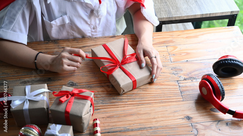 Cropped shot young woman opening Christmas gift box on wooden table.