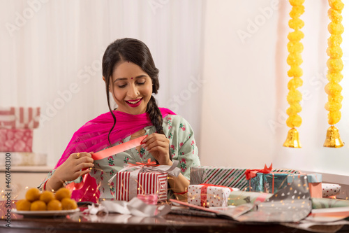 A woman holding ribbon to wrap gift amidst presents,sweets,Diwali light and festive garland decoration. photo