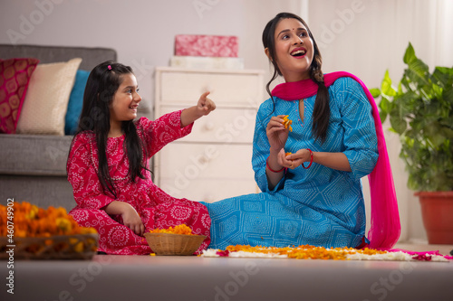 Daughter pointing something to her mother while decorating house with marigold flowers photo