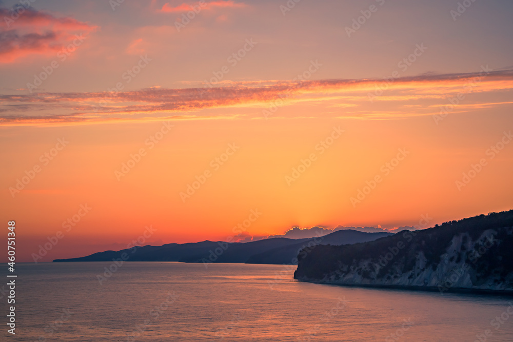 colorful sunset in the bright sky on the sea coast the sun has set behind the mountains in the bay and illuminates the clouds with reflections of the sun on the water