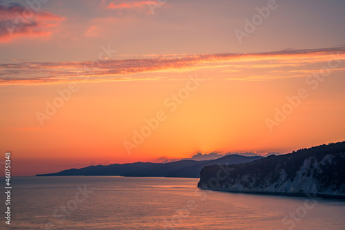 colorful sunset in the bright sky on the sea coast the sun has set behind the mountains in the bay and illuminates the clouds with reflections of the sun on the water