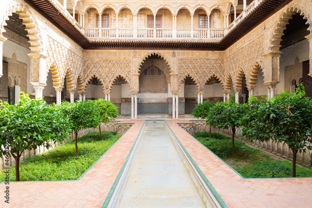 Water basin in a beautiful patio with green plants and arab style decorated arches in the famous Alcazar (meaning: fortress), Seville, Andalusia, Spain.