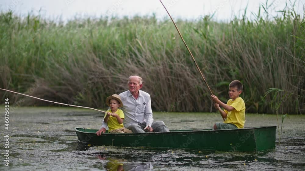 grandfather and grandsons fishing together on lake, family with sticks in boat on the background of reeds grandfather and grandsons fishing together on lake, family with sticks in boat on the background of reeds