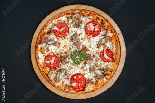 Pizza with meat and tomatoes on black background, top view.