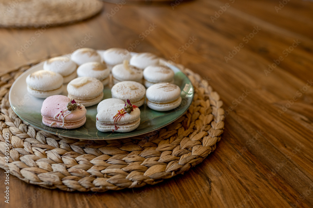White and pink macarons lie on a plate on a wooden table. Delicious light cookies on a brown background. Bakery. Valentine's Day background White and pink macarons lie on a plate on a wooden table. Delicious light cookies on a brown background. Bakery. Valentine's Day background