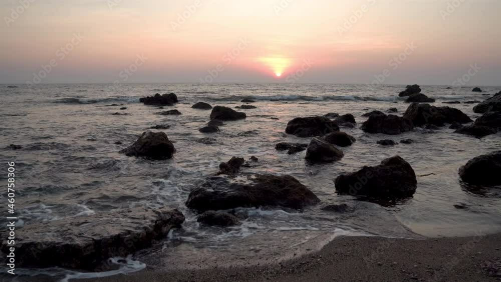 Handheld wide shot of a rocky coastline with waves on the rocks and sunset on the horizon Handheld wide shot of a rocky coastline with waves on the rocks and sunset on the horizon