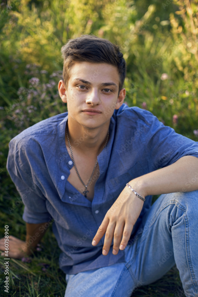 sexy teen guy sitting on the grass in nature in a shirt and jeans sexy teen guy sitting on the grass in nature in a shirt and jeans