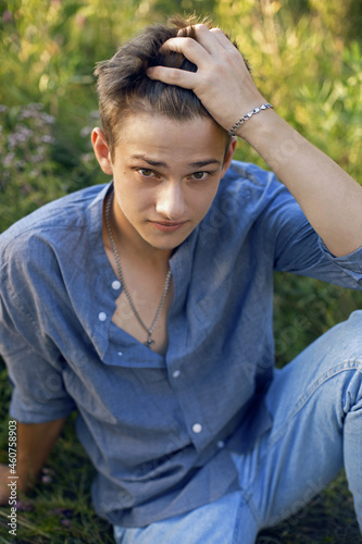 sexy teen guy sitting on the grass in nature in a shirt and jeans