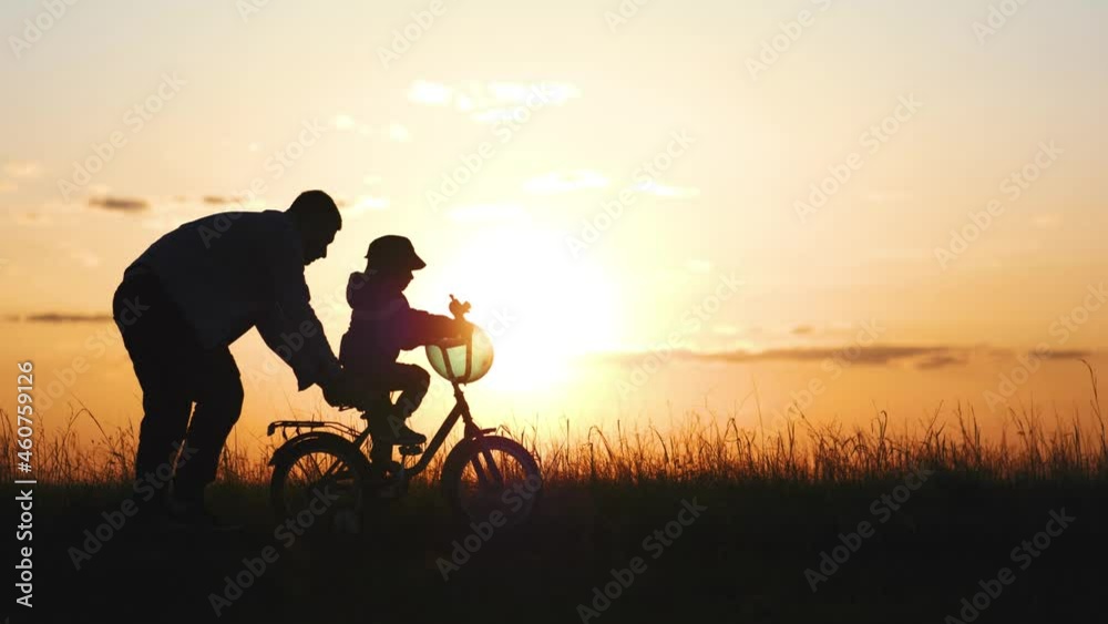 Happy family. Silhouette of a young family with a little son. Kid is learning to ride a bike. Silhouettes family with the child stand in a sunset. Teamwork, holding hands. Happy family concept. Happy family. Silhouette of a young family with a little son. Kid is learning to ride a bike. Silhouettes family with the child stand in a sunset. Teamwork, holding hands. Happy family concept.