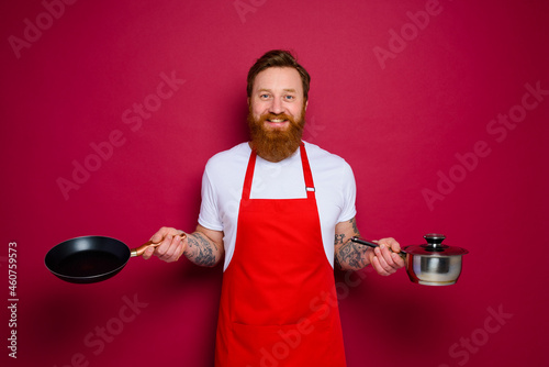 Fotótapéta Happy chef with beard and red apron cooks with pan and pot