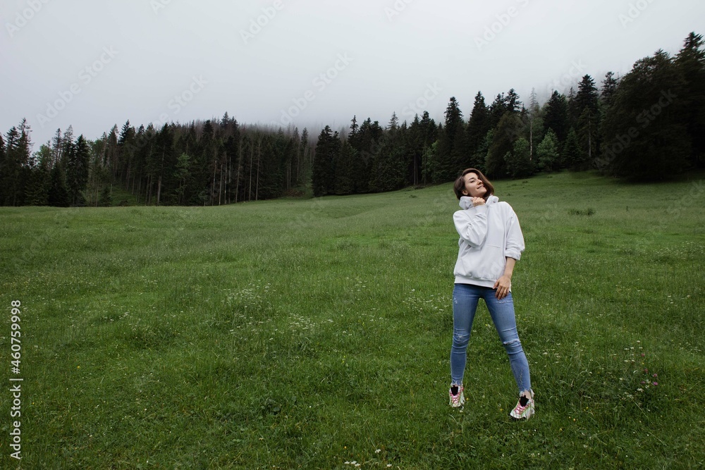 Woman traveler standing on a glade high in the mountains in front of forest, space for text, atmospheric epic moment
