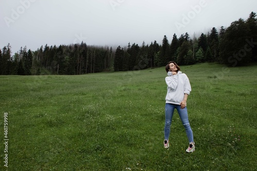 Woman traveler standing on a glade high in the mountains in front of forest, space for text, atmospheric epic moment