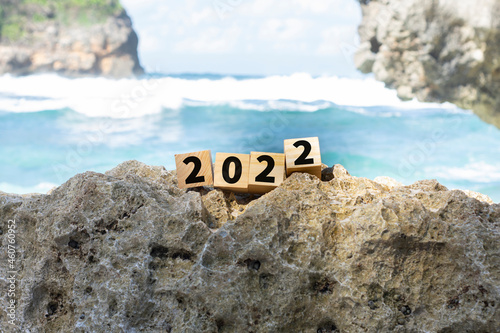 2022 is written on wooden cubes stacked on the rocks by the beach.