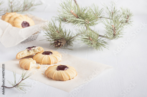 Christmas cookies with sweet red jam on white wood table decorated pine branches in soft light kitchen interior, copy space.